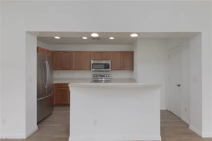 Kitchen with light countertops, appliances with stainless steel finishes, recessed lighting, brown cabinetry, and a kitchen island