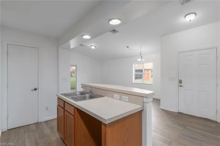 Kitchen with a center island with sink, light countertops, light wood-type flooring, brown cabinetry, and lofted ceiling