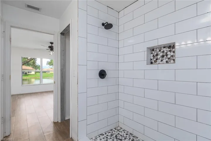 Bathroom featuring a shower stall, a ceiling fan, wood finished floors, and a water view