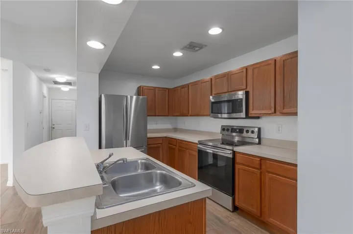 Kitchen featuring appliances with stainless steel finishes, brown cabinetry, light wood-style flooring, light countertops, and recessed lighting