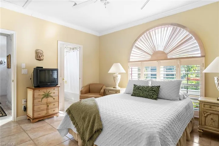 Tiled bedroom featuring ensuite bathroom, ceiling fan, and ornamental molding