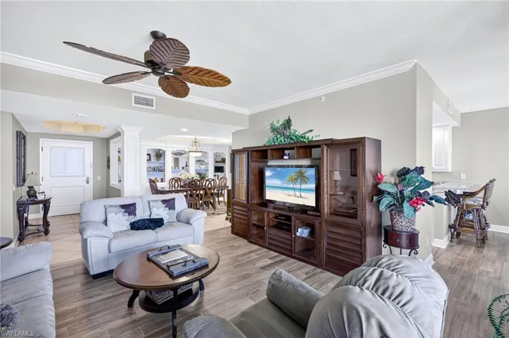 Living room with crown molding, wood finished floors, decorative columns, and a ceiling fan