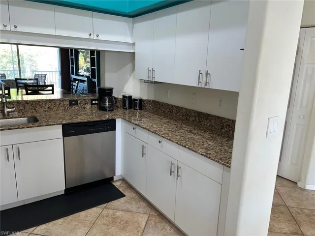 Kitchen featuring white cabinets, dishwasher, dark stone countertops, and light tile patterned floors