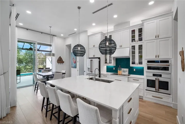 Kitchen with a kitchen island with sink, sink, high end fridge, decorative light fixtures, and stainless steel double oven