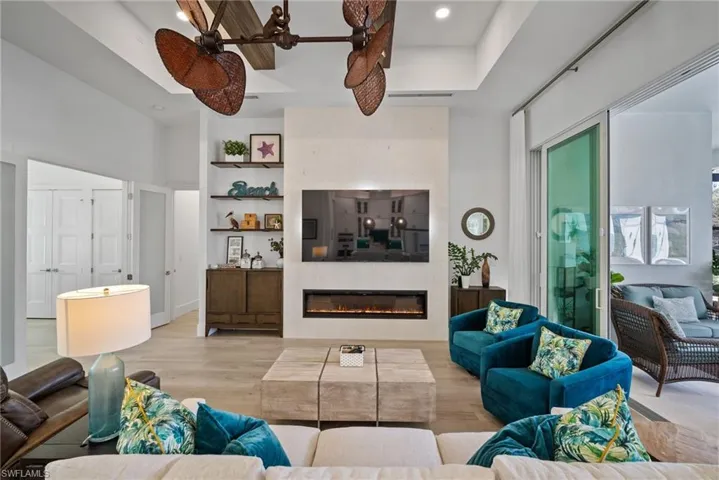 Living room featuring a large fireplace, a raised ceiling, light hardwood / wood-style floors, and ceiling fan