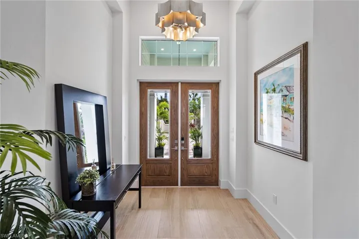 Foyer entrance featuring french doors, a notable chandelier, a towering ceiling, and light hardwood / wood-style flooring