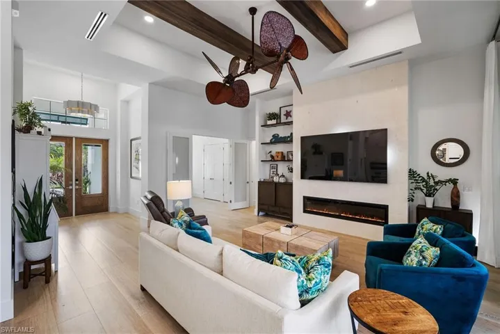 Living room with a towering ceiling, light wood-type flooring, a fireplace, french doors, and beam ceiling