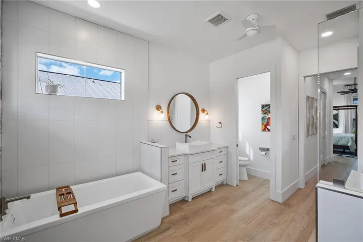 Bathroom with a tub, hardwood / wood-style floors, toilet, ceiling fan, and vanity