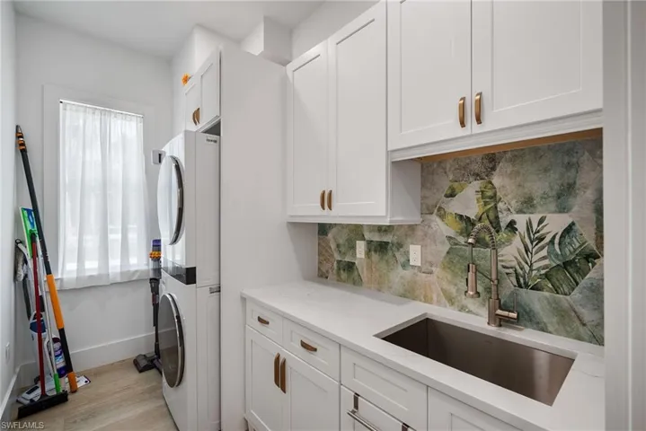 Laundry area featuring cabinets, light hardwood / wood-style flooring, stacked washer and dryer, and sink
