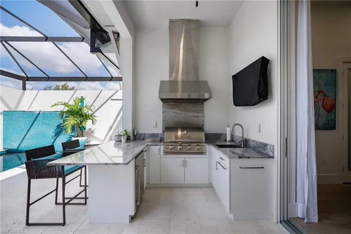View of patio / terrace featuring exterior kitchen, area for grilling, glass enclosure, and an outdoor wet bar