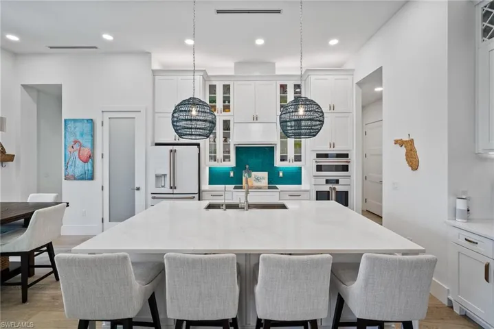 Kitchen featuring light stone counters, an island with sink, high end white fridge, multiple ovens, and sink