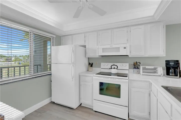 Kitchen with white appliances, crown molding, white cabinetry, light countertops, and light wood-style floors