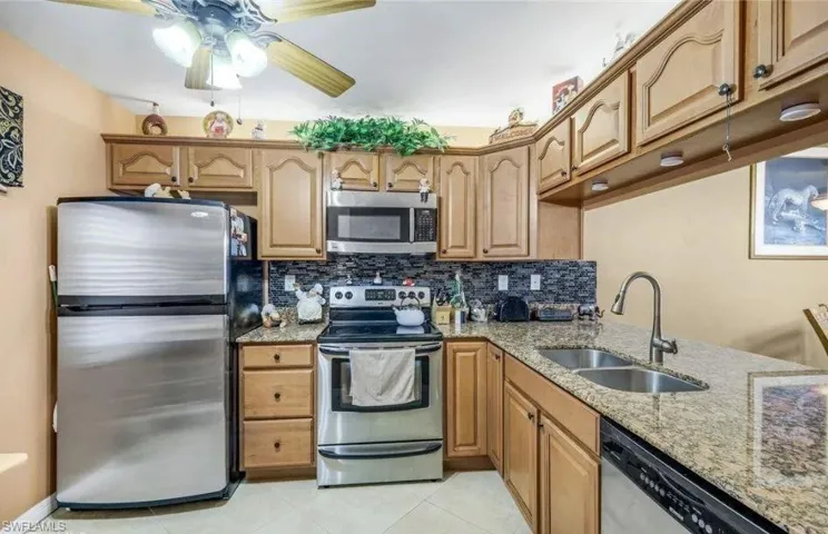 Kitchen featuring stainless steel appliances, light stone counters, ceiling fan, backsplash, and light tile patterned floors