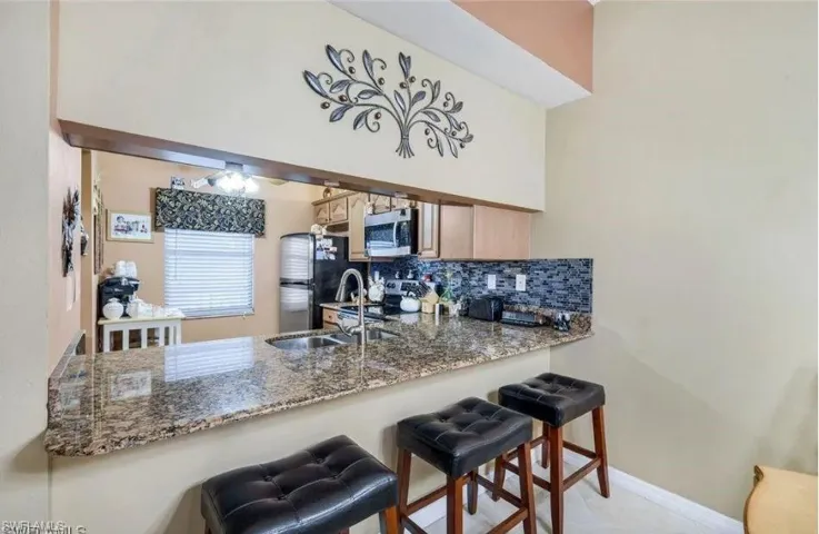 Kitchen with a breakfast bar, a peninsula, tasteful backsplash, stainless steel appliances, and dark stone countertops