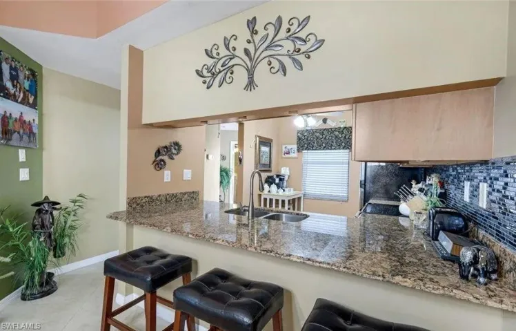 Kitchen with a kitchen bar, dark stone countertops, decorative backsplash, and a peninsula