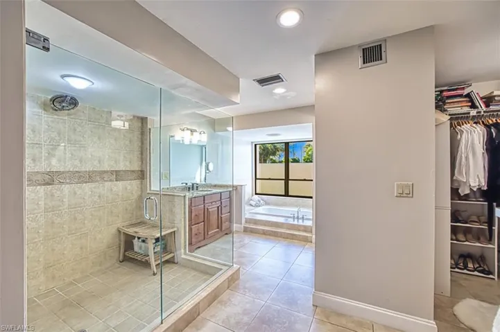 Full bathroom featuring vanity, a shower stall, a walk in closet, a bath, and light tile patterned floors