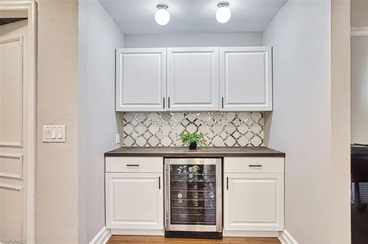 Bar featuring wine cooler, white cabinetry, and backsplash