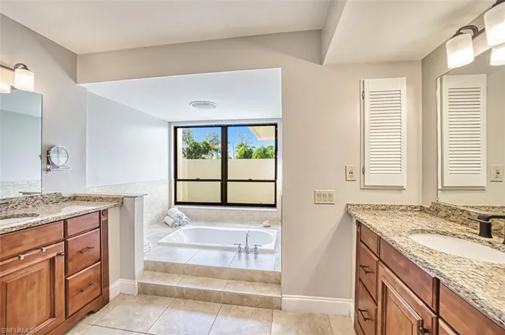 Bathroom featuring two vanities, a garden tub, and light tile patterned flooring