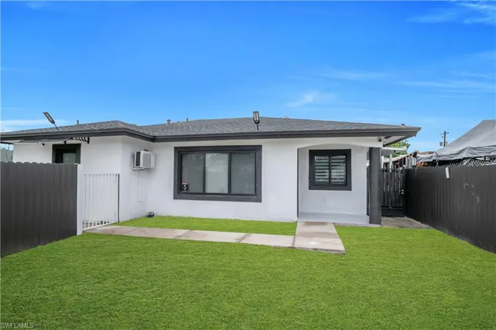 White stucco exterior with dark trim windows, covered entry, and dark fencing
