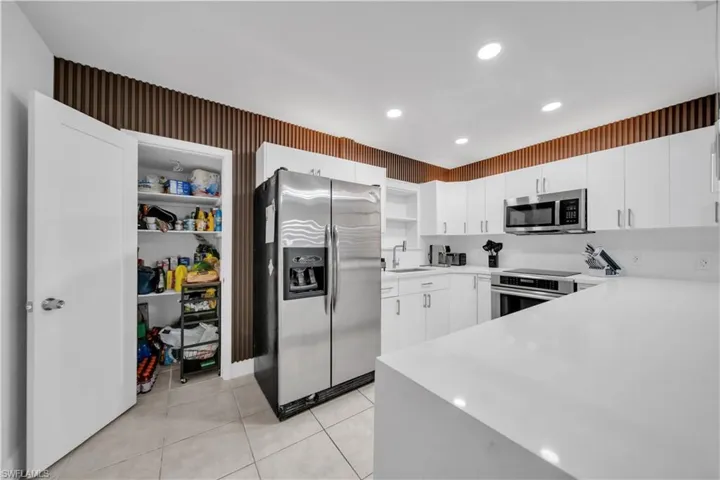 Modern kitchen featuring white cabinetry, integrated stainless steel appliances, extensive white countertops, a large pantry, and recessed lighting
