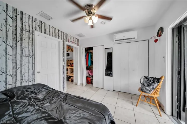 Room featuring tree-patterned accent wall, white paneled doors, ceiling fan with integrated lighting, and ceramic tile flooring