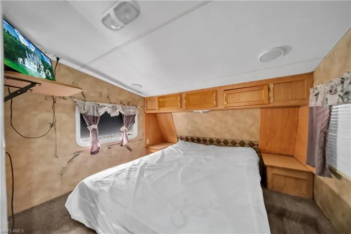 Sleeping area featuring built-in cabinetry, a wall-mounted television, and a window with valance and drapes