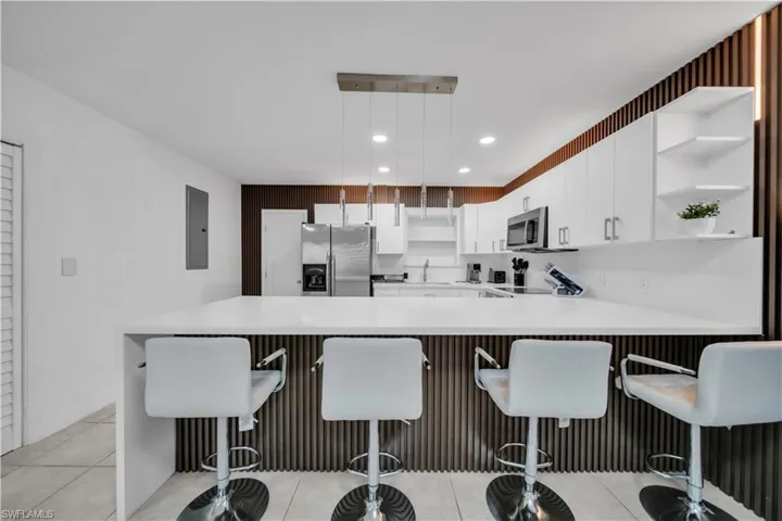 Modern kitchen featuring a white countertop island with integrated seating, white cabinetry, stainless steel appliances, and a unique slatted accent wall with integrated lighting