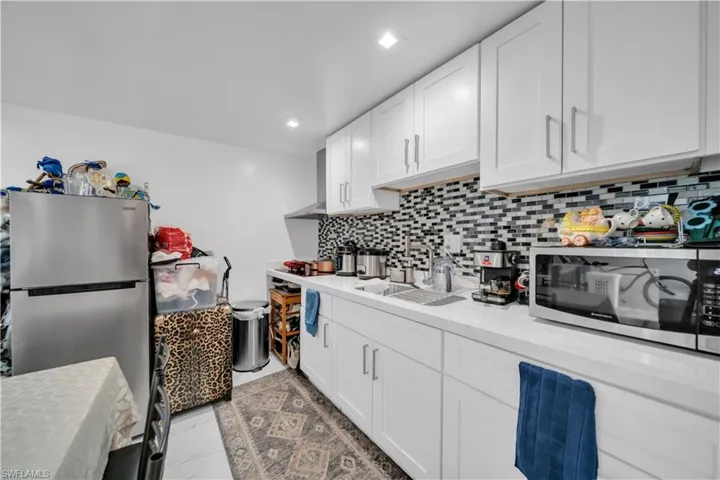 Modern kitchen featuring white shaker cabinetry, stainless steel sink, tile backsplash with a mosaic pattern, white countertops, and recessed lighting