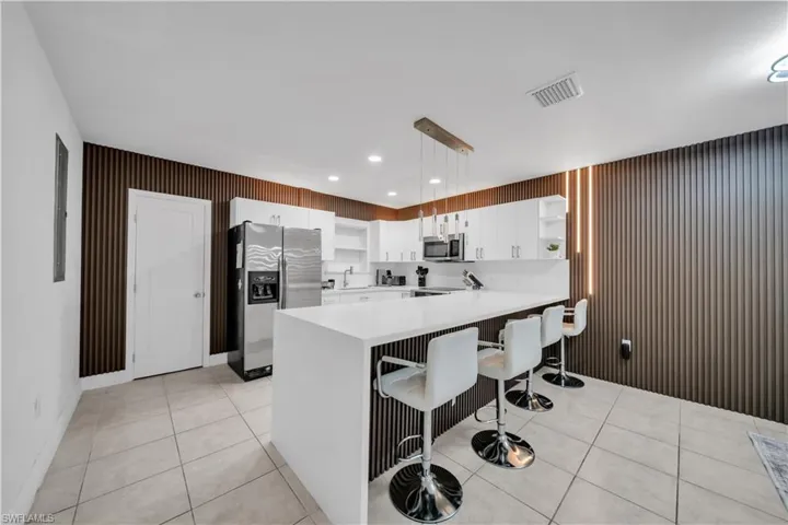 Modern kitchen featuring white cabinetry, a large center island with seating, stainless steel appliances, and a unique slatted accent wall with integrated lighting