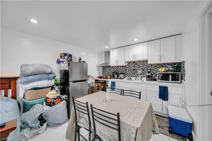 Kitchen featuring white cabinetry, a patterned tile backsplash, stainless steel range hood, white countertops, and recessed lighting