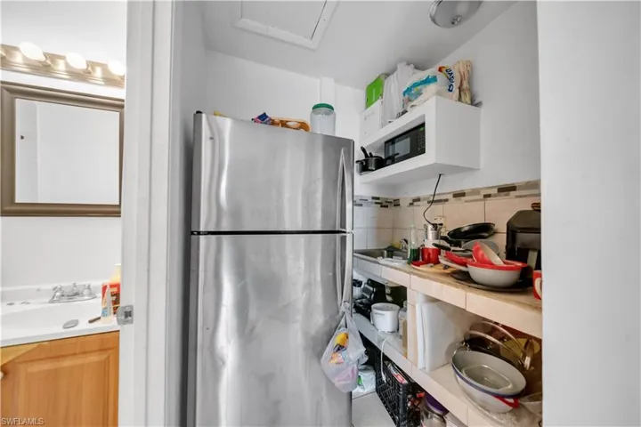 Compact kitchen area featuring a stainless steel refrigerator, white floating shelving, and a tiled backsplash
