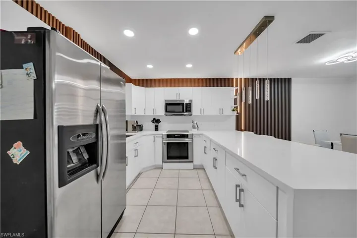 Modern kitchen featuring an expansive countertop island, white cabinetry, stainless steel appliances, recessed lighting, and tile flooring
