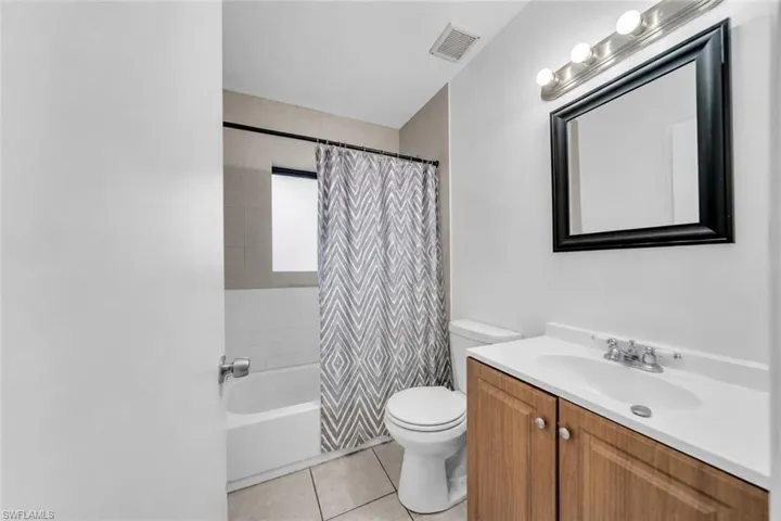 Bathroom featuring a wood-finish vanity with an integrated sink, a rectangular framed mirror, and a full bathtub with tile surround