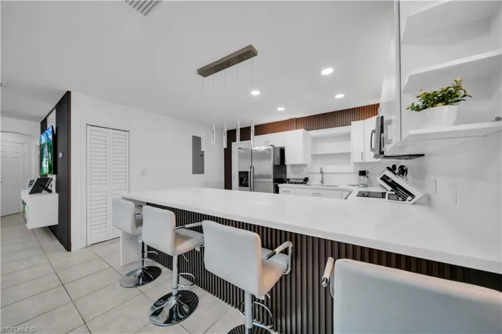 Contemporary kitchen featuring a large white countertop island with integrated seating, white cabinetry, open shelving, and stainless steel appliances
