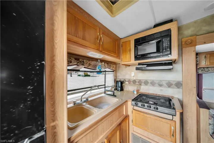 Kitchenette featuring wood-finish cabinetry, a double basin sink, a compact stovetop, and an overhead microwave with a range hood