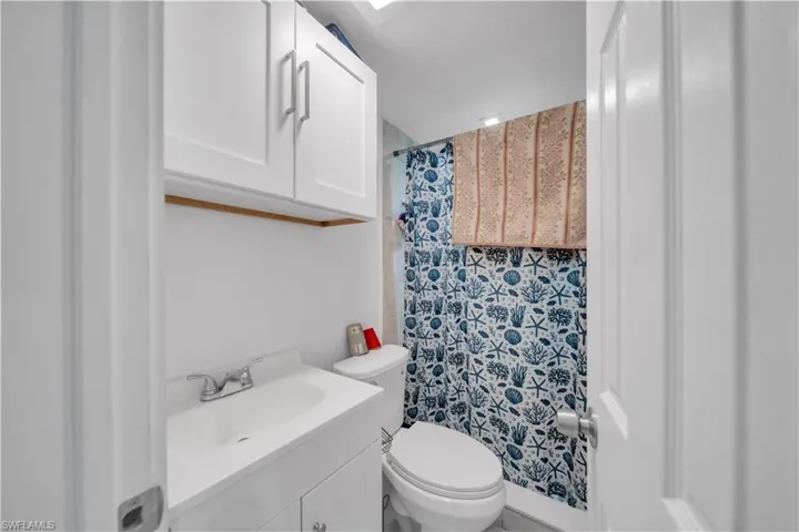 Compact bathroom featuring a white vanity with integrated sink, chrome faucet, and overhead cabinetry