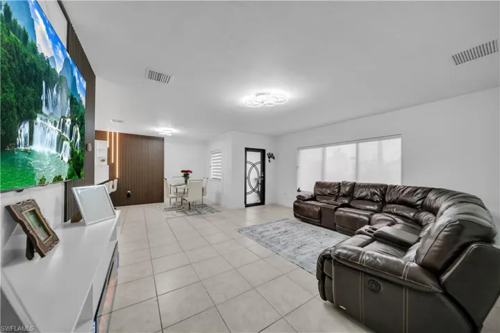 Expansive open-concept living area featuring light-toned tile flooring, white walls, and a contemporary ceiling light fixture