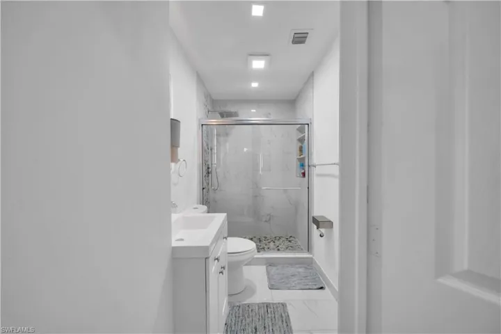 Full bathroom with a glass-enclosed shower, white vanity cabinet, rectangular sink, and tile flooring