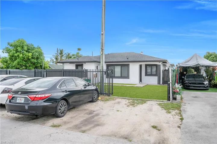 White exterior residence with dark trim windows, featuring a fenced front yard with a manicured green lawn and a paved driveway