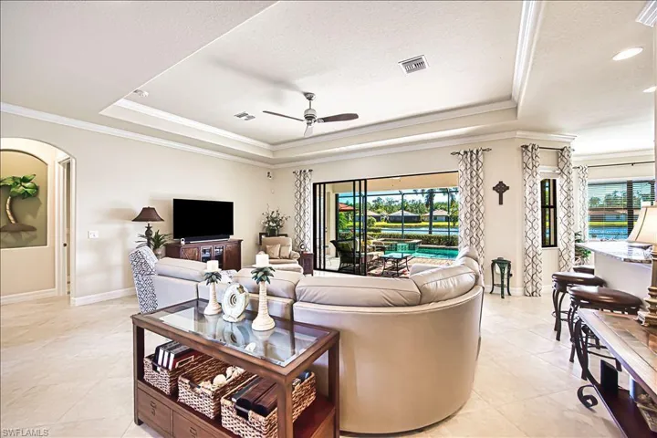 Living area featuring ceiling fan, a tray ceiling, visible vents, and ornamental molding