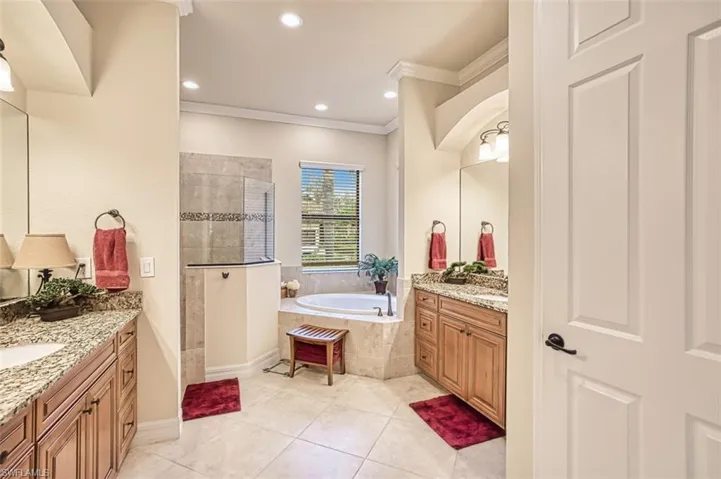 Bathroom featuring tile patterned floors, a garden tub, two vanities, ornamental molding, and walk in shower