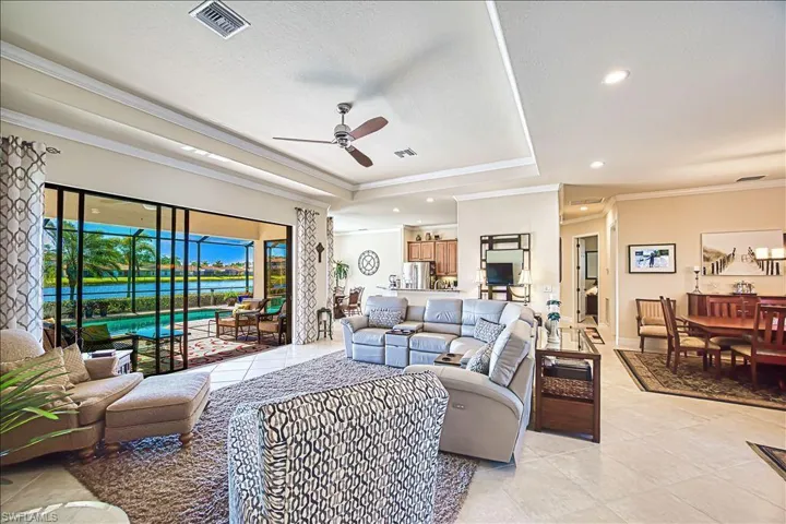 Living area featuring light tile patterned floors, a ceiling fan, visible vents, crown molding, and a raised ceiling