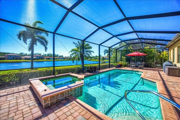 View of swimming pool with glass enclosure, a patio, a water view, and a pool with connected hot tub