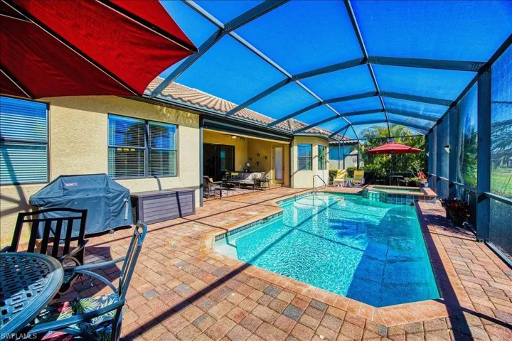 View of swimming pool with area for grilling, glass enclosure, a pool with connected hot tub, and a patio area