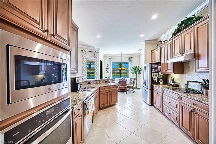 Kitchen with under cabinet range hood, tasteful backsplash, appliances with stainless steel finishes, crown molding, and light tile patterned floors