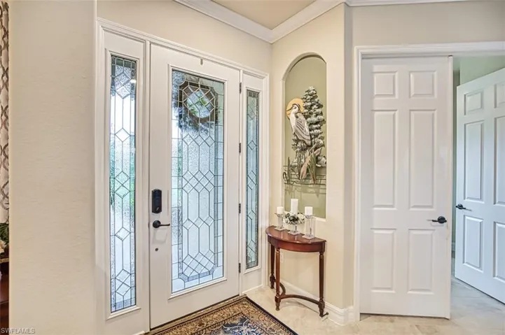 Entrance foyer with crown molding, light tile patterned floors, and a textured wall