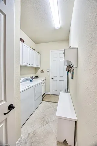 Laundry room featuring independent washer and dryer, a textured ceiling, cabinet space, light tile patterned floors, and a laundry tub sink