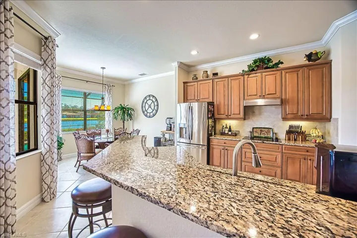 Kitchen with under cabinet range hood, stainless steel fridge with ice dispenser, light tile patterned floors, decorative backsplash, and light stone countertops