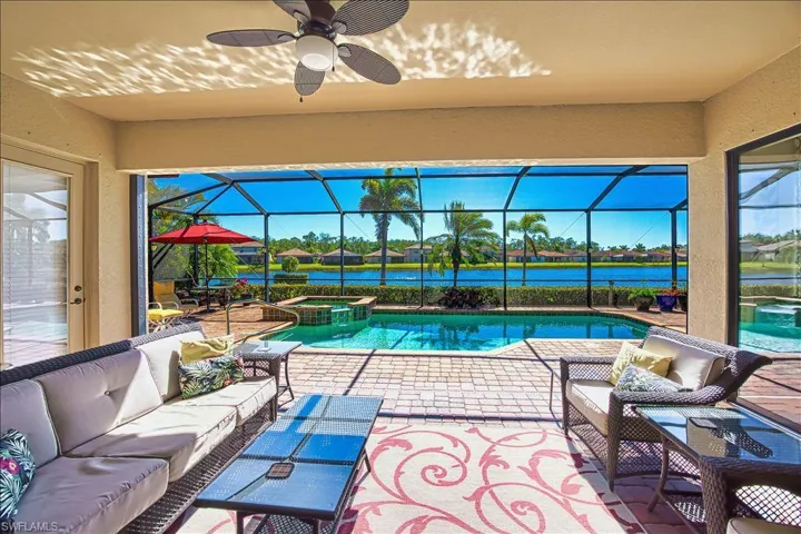View of swimming pool featuring glass enclosure, a patio, a pool with connected hot tub, a water view, and outdoor lounge area