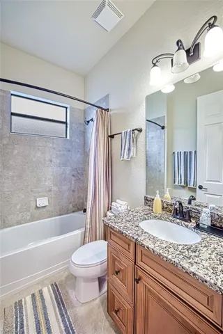 Bathroom featuring tile patterned flooring, toilet, shower / bath combination with curtain, and vanity